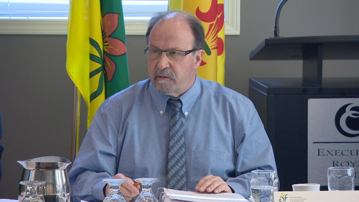 Le président de l'ACF, Roger Gauthier, préside l'Assemblée des députés communautaires, assis devant les drapeaux de la Saskatchewan et fransaskois.