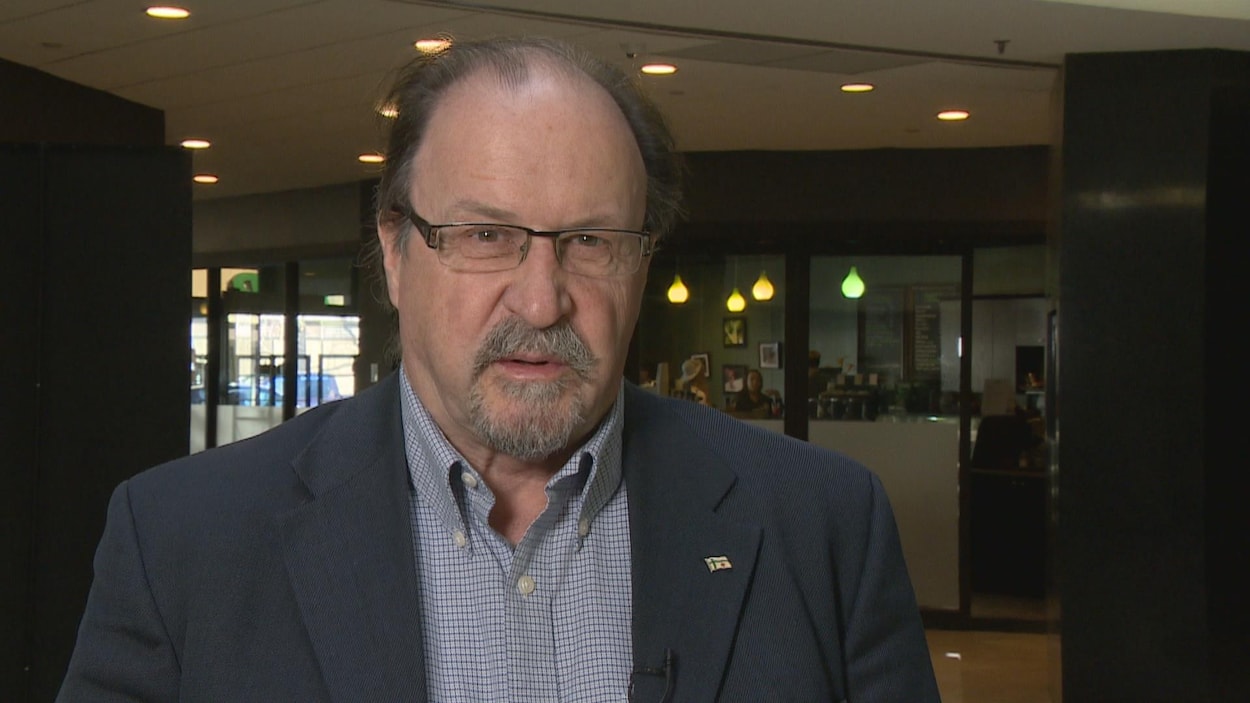 Roger Gauthier se trouve dans un corridor assez sombre. Il porte une chemise et un veston bleus. Roger Gauthier se trouve dans un corridor assez sombre. Il porte une chemise et un veston bleus.
