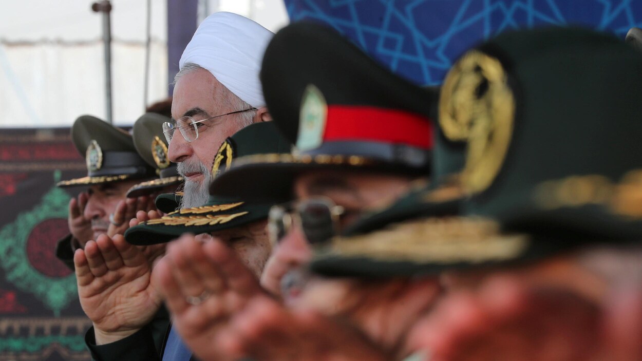 Hassan Rohani fait le salut militaire entouré d'officiers portant des casquettes.