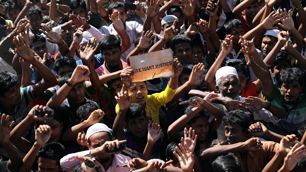 Une foule d'hommes dont la plupart ont les bras levés. Un de ceux-ci portent une pancarte portant l'inscription « We want justice» (Nous voulons que justice soit faite».