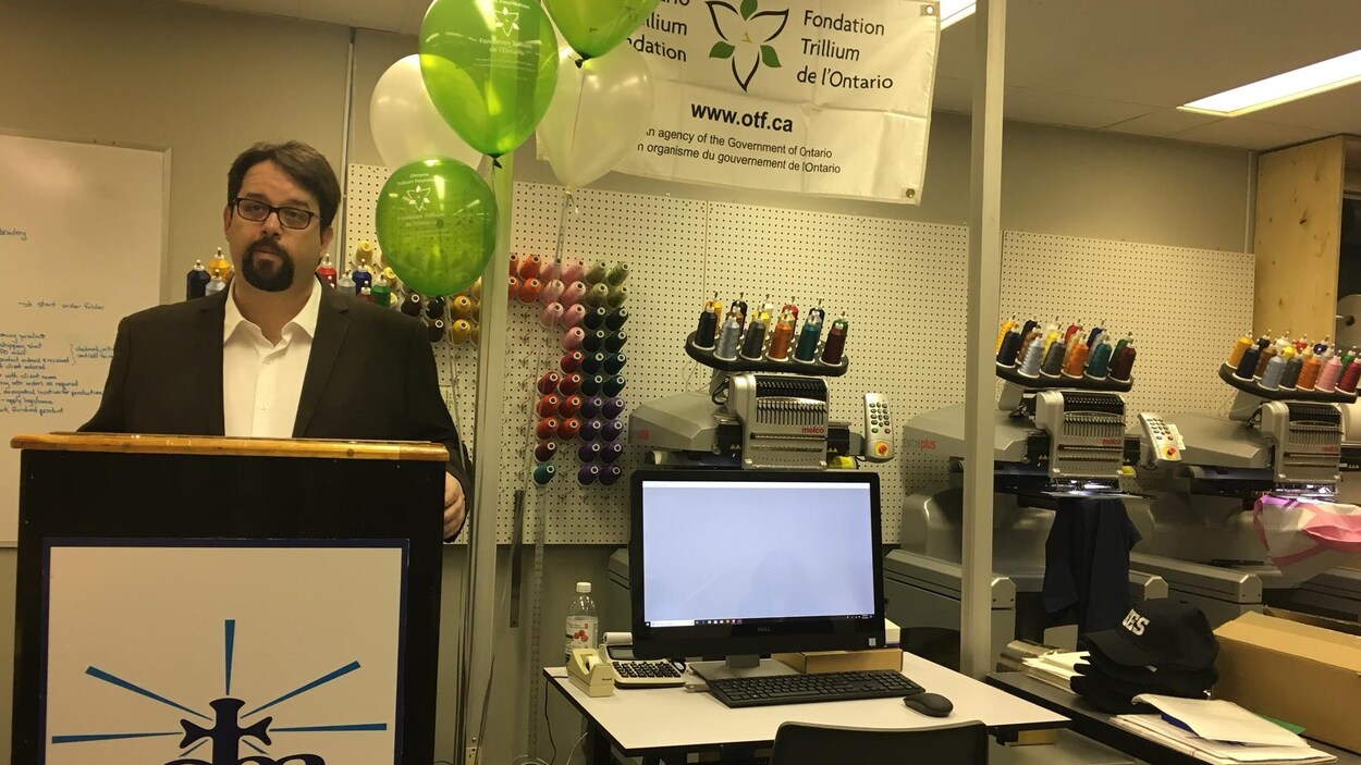 Le directeur se tient dans un atelier de couture où sont disposés des ballons et une affiche de la Fondation Trillium de l'Ontario.