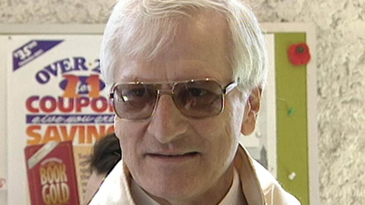 Un homme aux cheveux blancs portant des lunettes regarde vers la droite