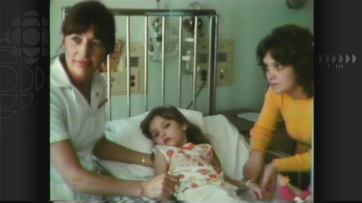 La jeune Caroline accompagnée de sa mère (à droite) et d'une infirmière (à gauche) sur un lit d'hôpital.