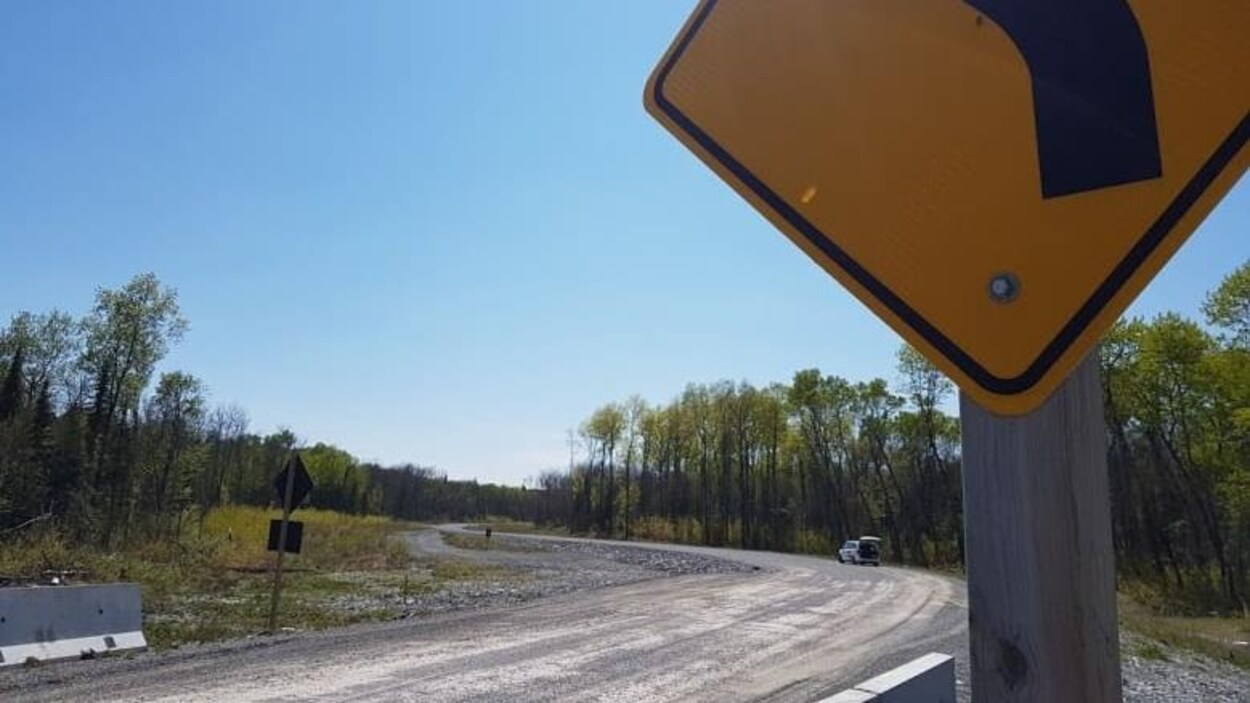 Un panneau est positionné devant une route qui traverse des terrains forestiers.