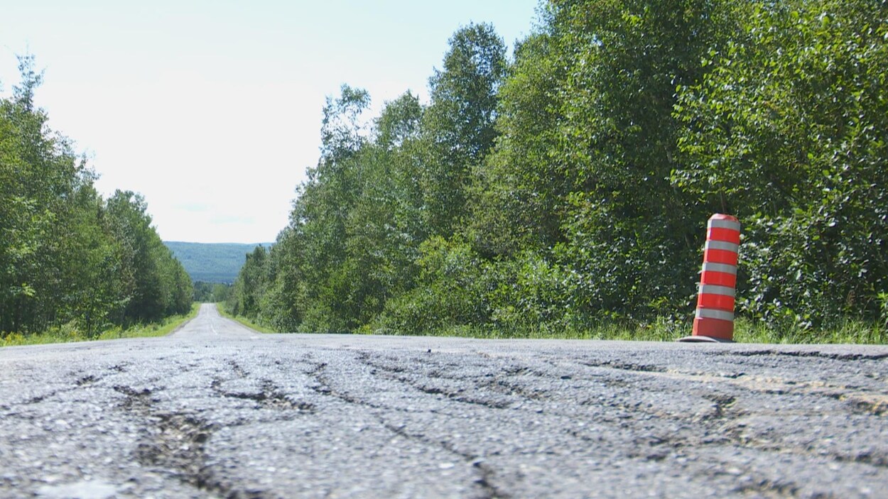 Une route asphaltée abîmée avec un cône orange.
