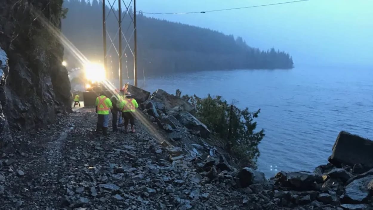Des ouvriers sur une route remplie de gros cailloux le long d'un lac.