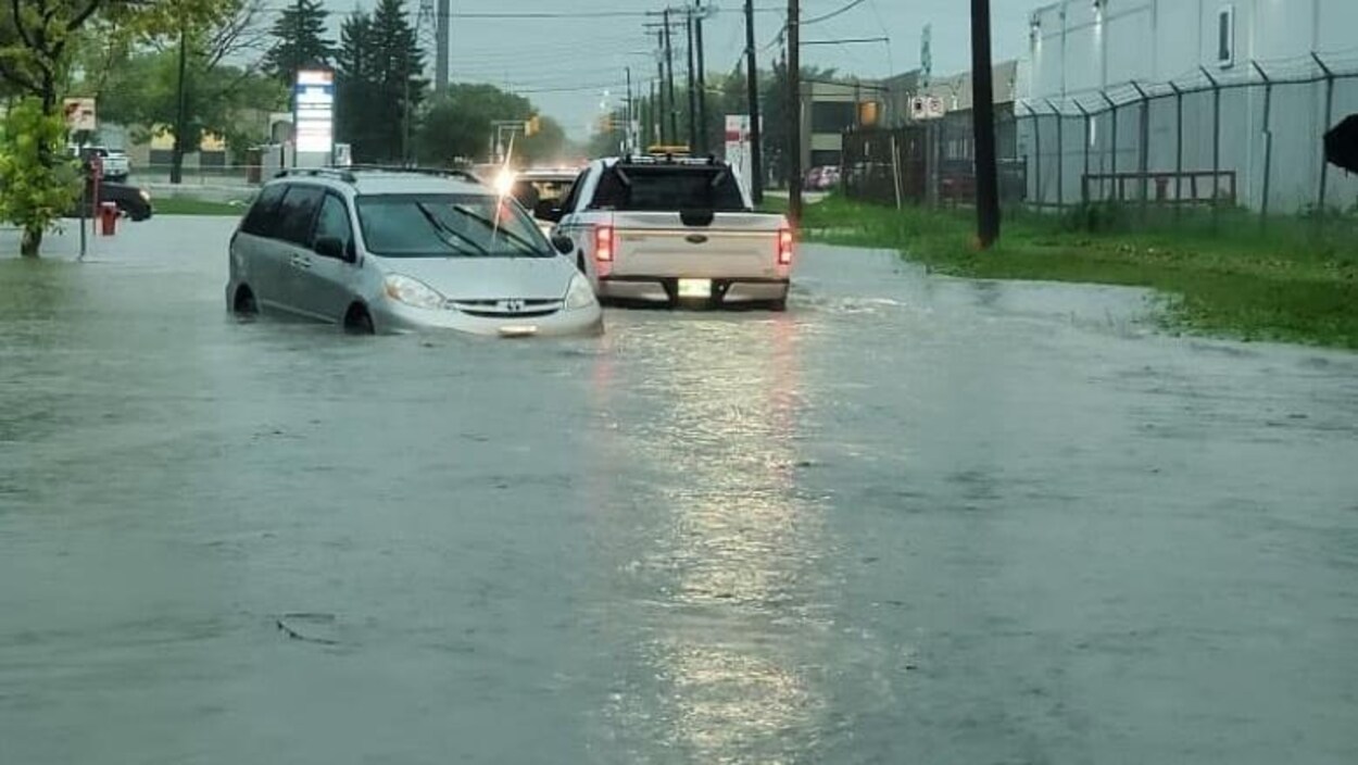 Des véhicules roulent dans une rue avec de l'eau à hauteur des portières.