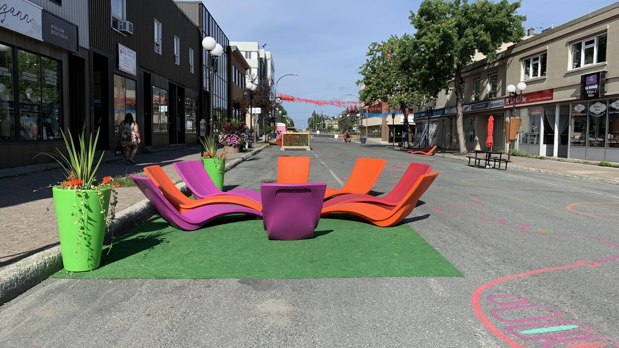 Des bancs colorés installés dans la rue, avec des dessins sur l’asphalte et des banderoles au dessus du trottoir.