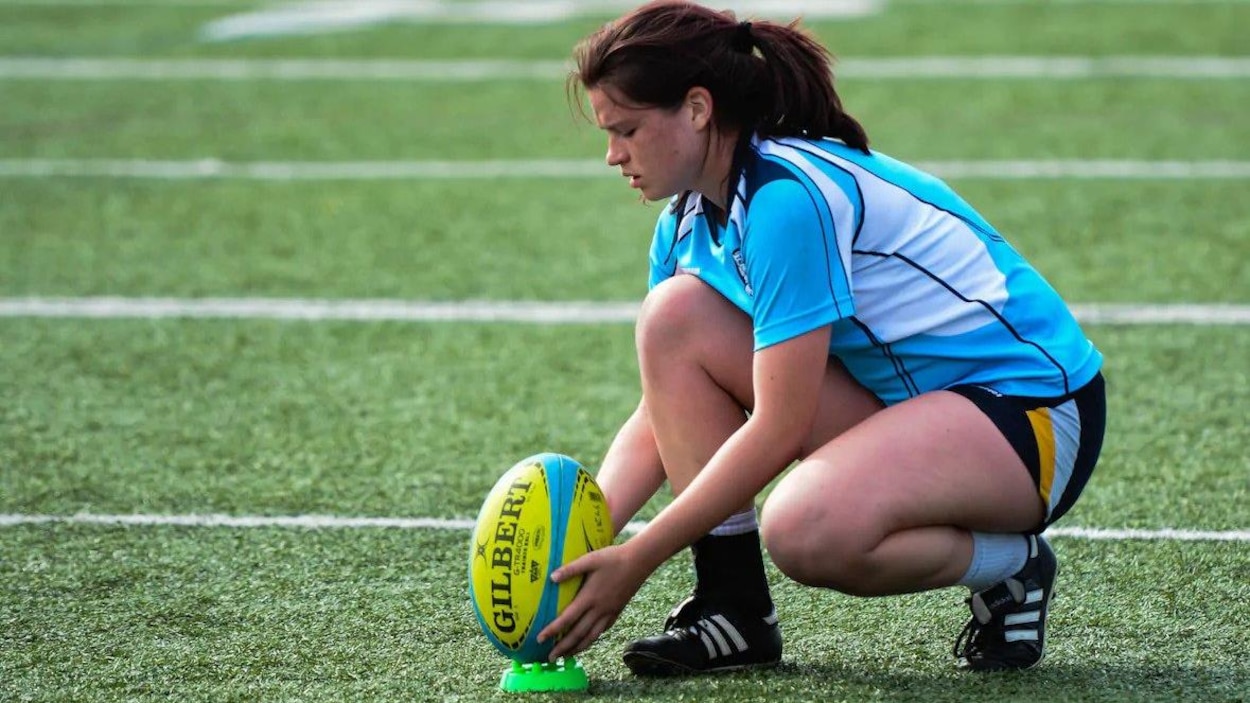 Joueuse de rugby agenouillée devant le ballon.