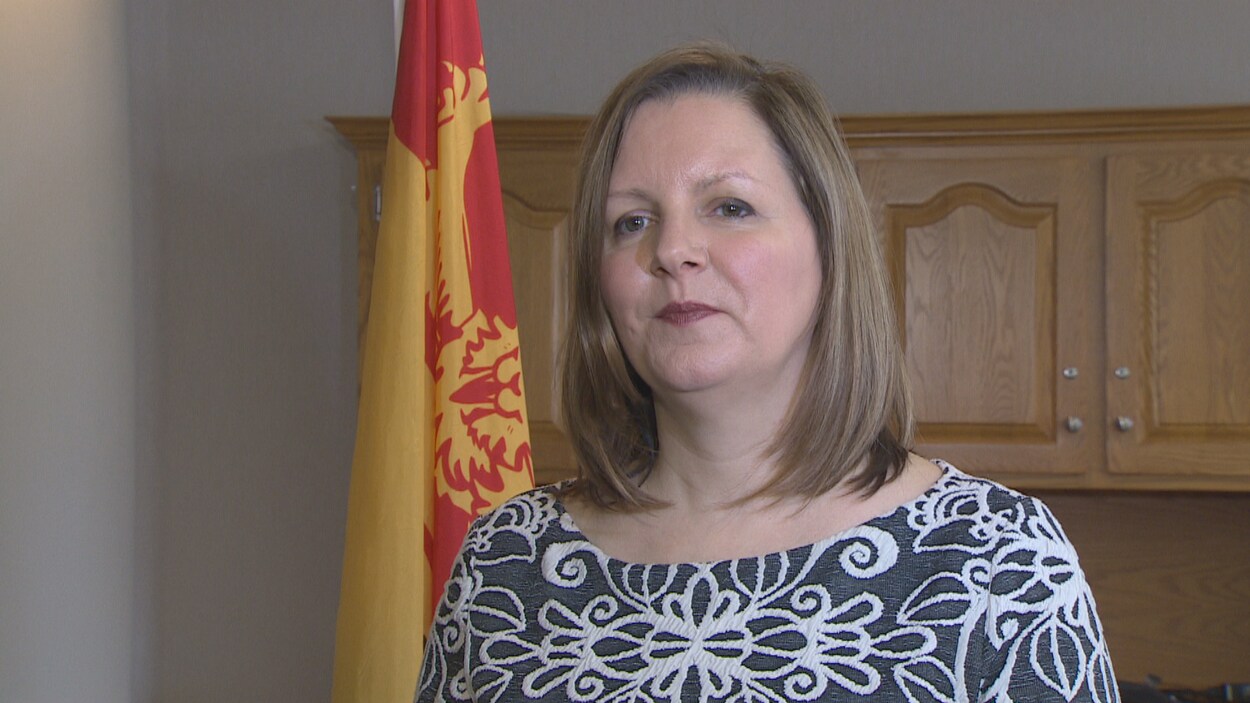 Jennifer Russell en entrevue devant un drapeau du Nouveau-Brunswick.