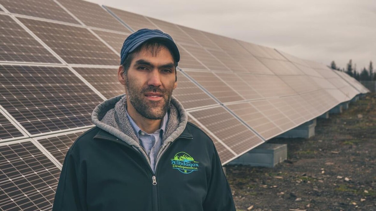 Plan moyen de Russell Myers Ross debout devant une rangée de panneaux solaires.