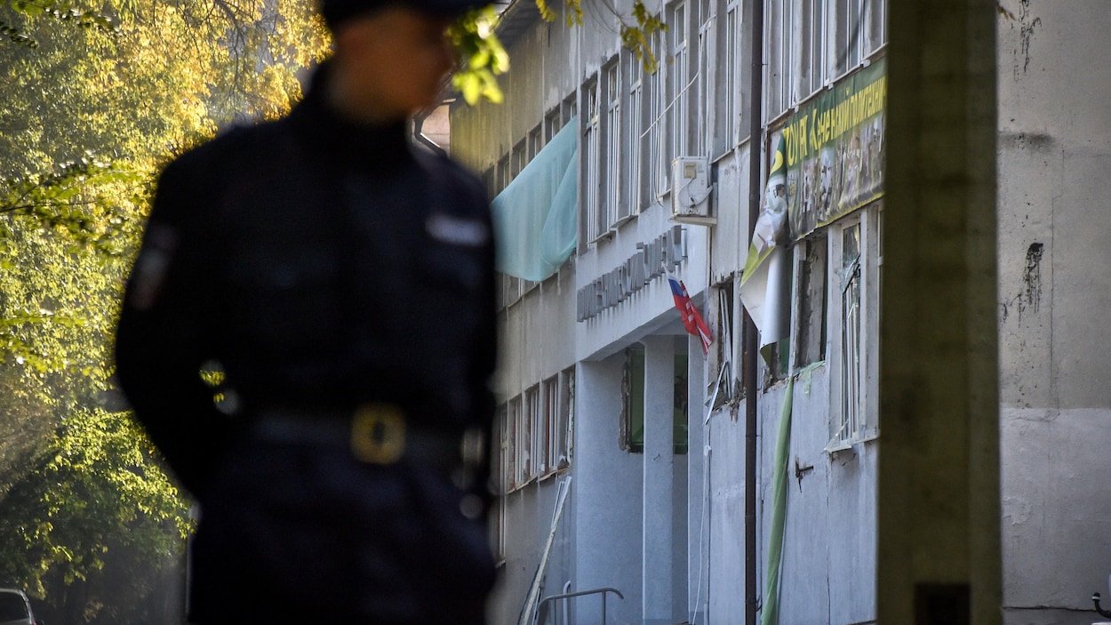 Un policier se tient debout, les mains derrière le dos, devant le collège technique de Kertch, en Crimée. Un policier se tient debout, les mains derrière le dos, devant le collège technique de Kertch, en Crimée.