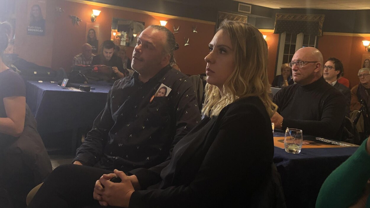 Ruth Ellen Brosseau avec son conjoint qui regarde au loin un écran.