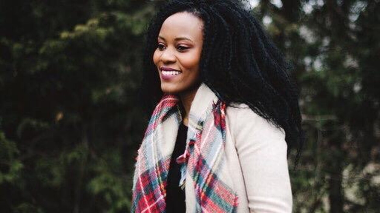 Ruth Maniriho Bansoba, souriante, avec un foulard et un veston rose pâle, à l'extérieur, le jour.