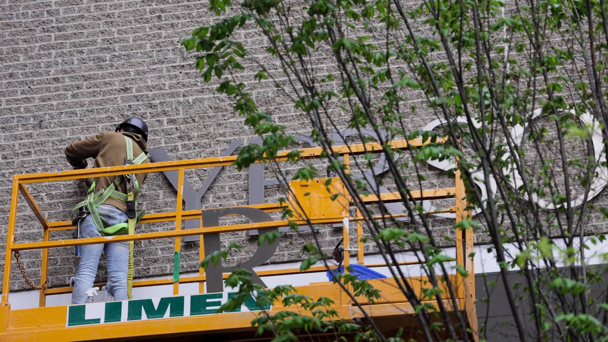 Un travailleur retire une enseignes Ryerson sur un édifice. 
