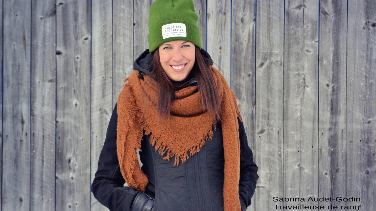 Une femme portant des vêtements d'hiver sourit à la caméra devant un mur de grange.