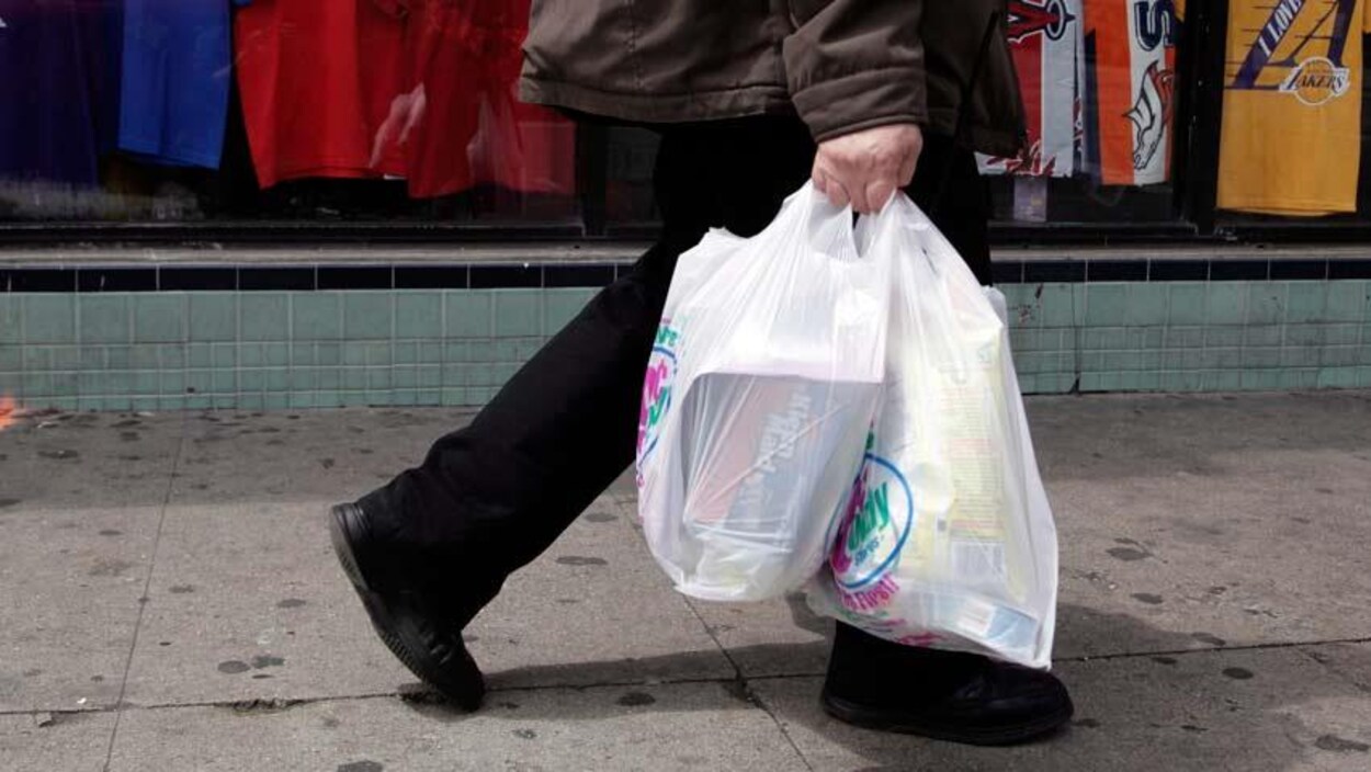 Un passant portant son épicerie dans des sacs jetables.