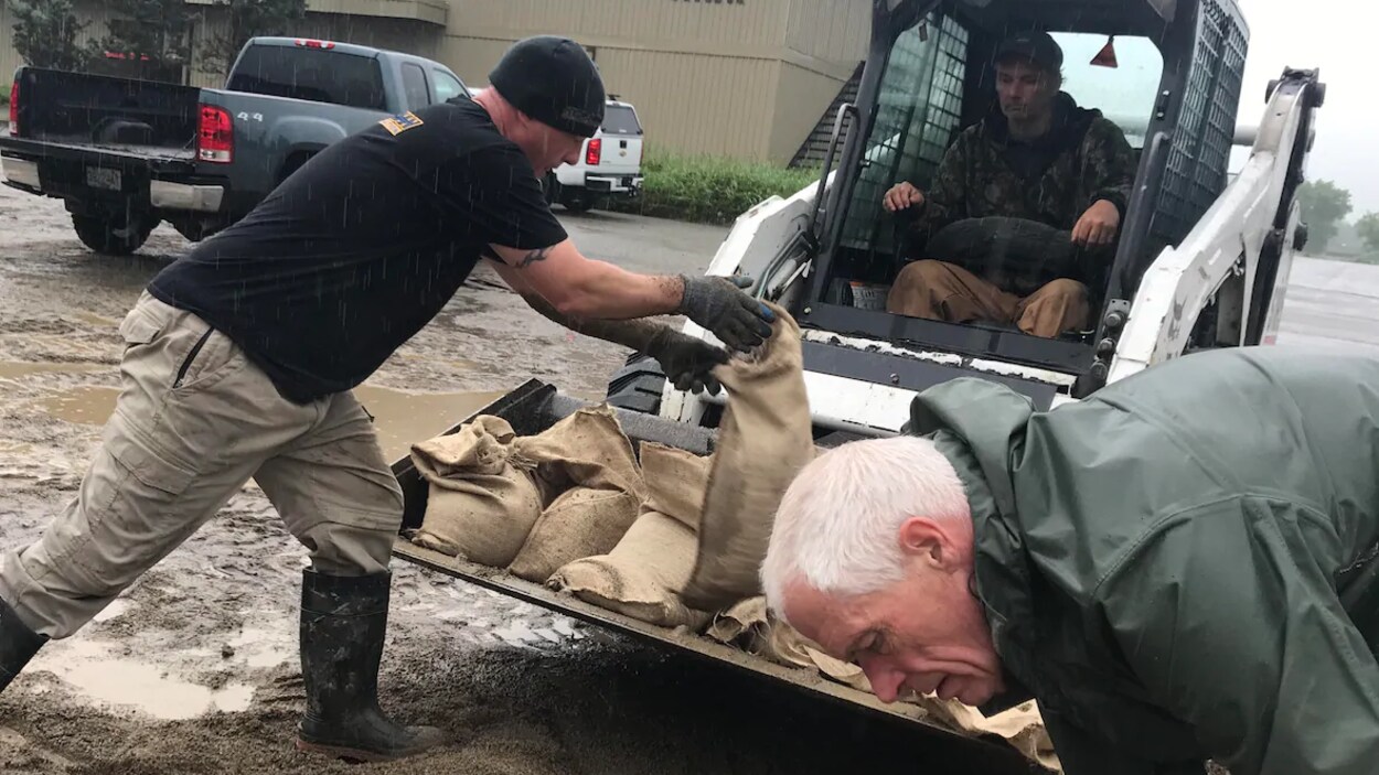 Des sacs de sable sont remplis par trois hommes dont un assis dans une petite pelle mécanique près de l'aréna de Grand Forks.