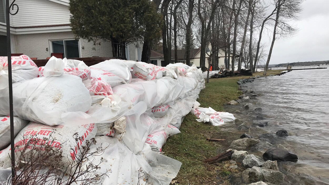 Des sacs de sable sont empilés aux abords d'un lac près de résidences.