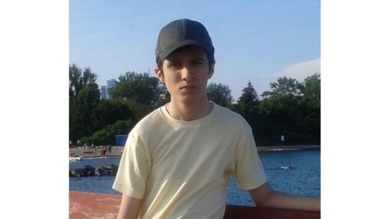 Un adolescent avec une casquette et un chandail jaune devant un lac.