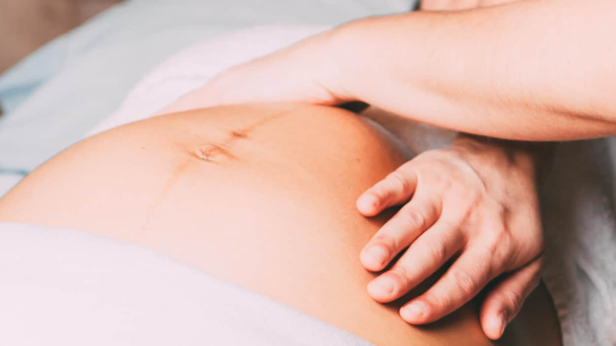 Deux mains de femme sur le ventre d'une femme enceinte couchée sur le dos.