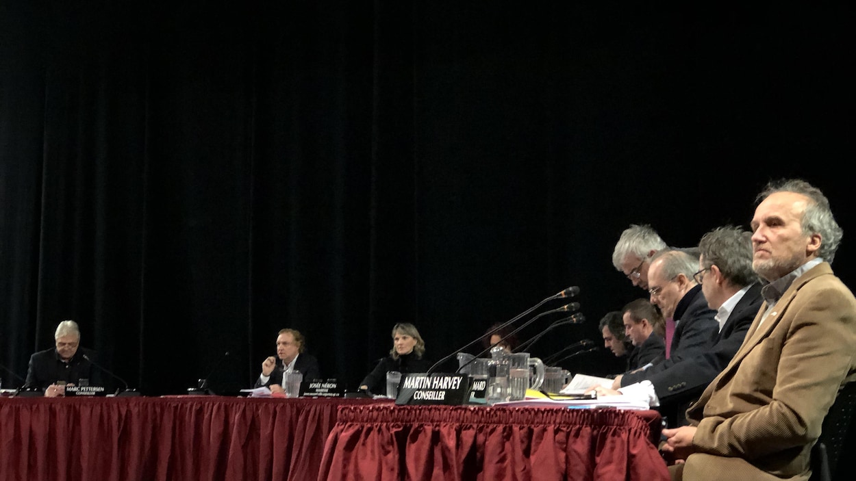 Des personnes assises à une table devant un rideau noir.