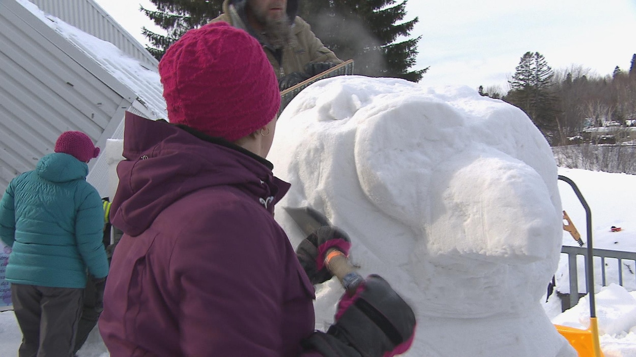 Une femme de dos en train de sculpter en bloc de neige.