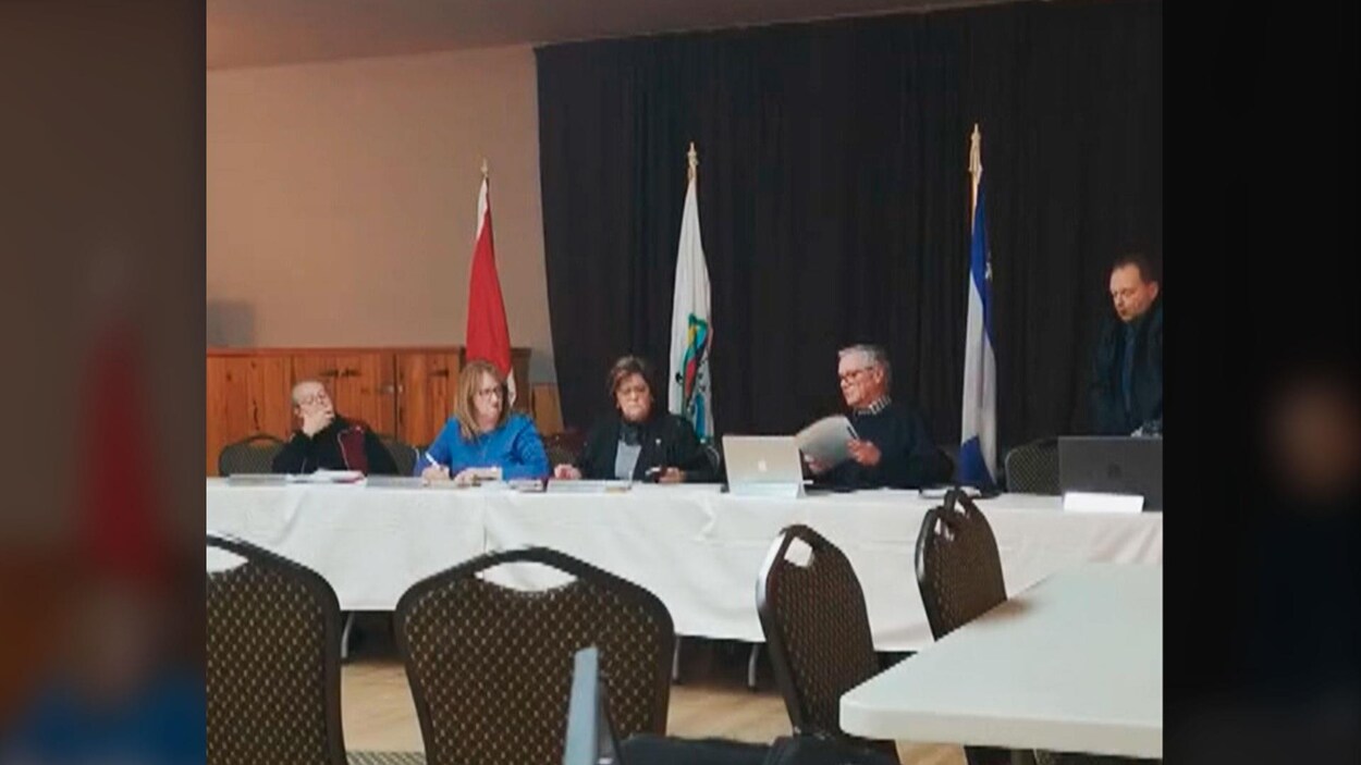 Quatre personnes assises autour d'une table avec une nappe blanche, tout le monde a un air très sérieux.