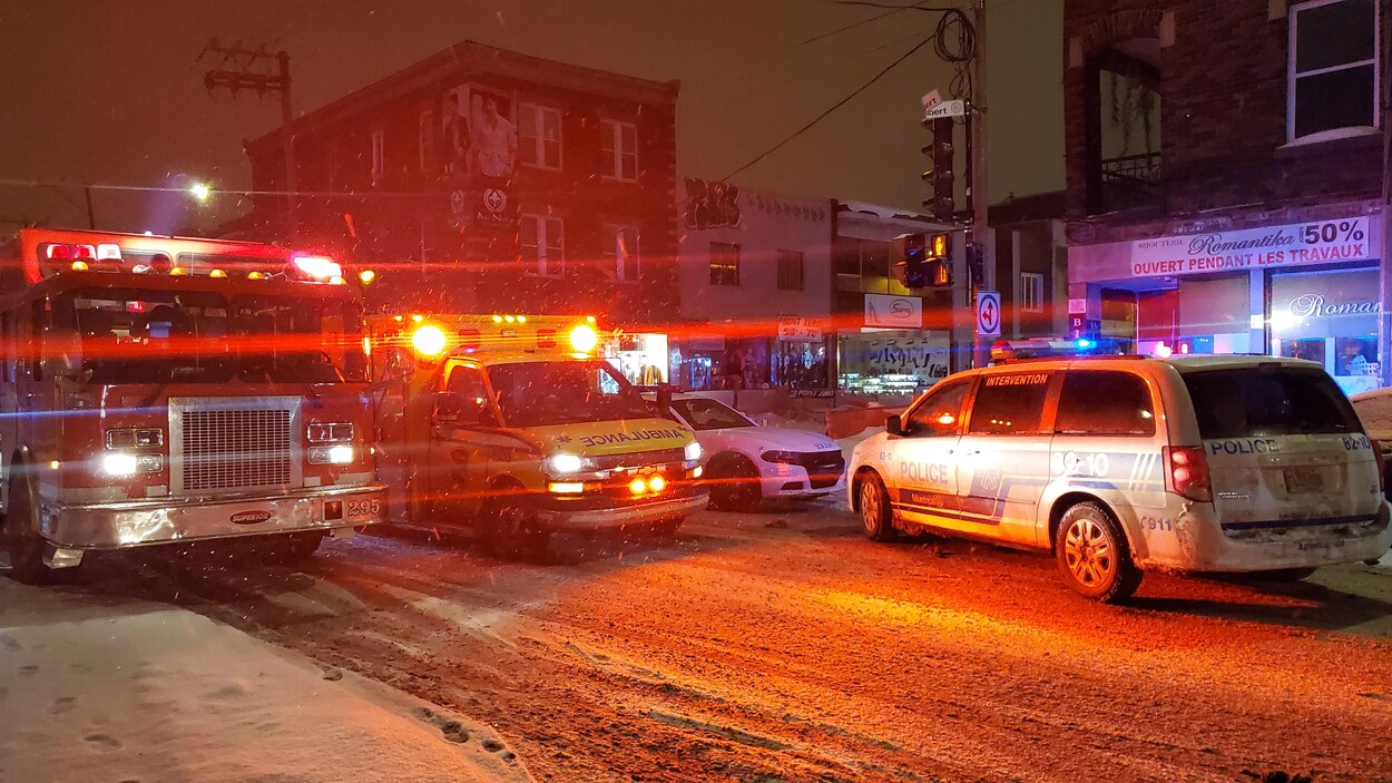 Des voitures de police, une ambulance et un camion de pompier à l'intersection de deux rues enneigées.