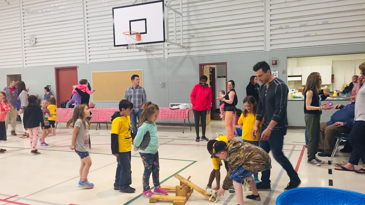 Des adultes et des enfants sont rassemblés dans un gymnase et vaquent à diverses activités.