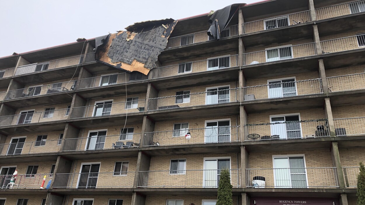 Un immense morceau de toiture pend renversé sur le bord d'un édifice à logements de six étages.