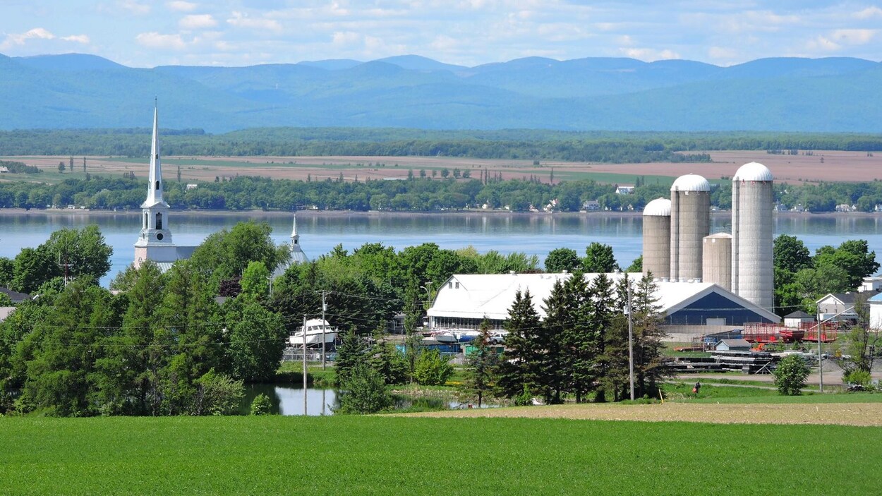 On voit les bâtiments agricoles et l'église du village de Saint-Michel-de-Bellechasse. Derrière, de l'autre côté du fleuve, on aperçoit l'île d'Orléans et au loin, les contreforts des montagnes du parc des Laurentides.