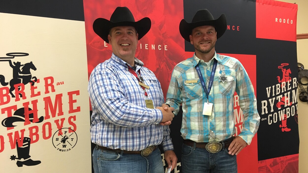 Deux hommes en chapeaux de cowboy et chemises à carreaux se serrent la main devant une toile du Festival western de Saint-Tite.
