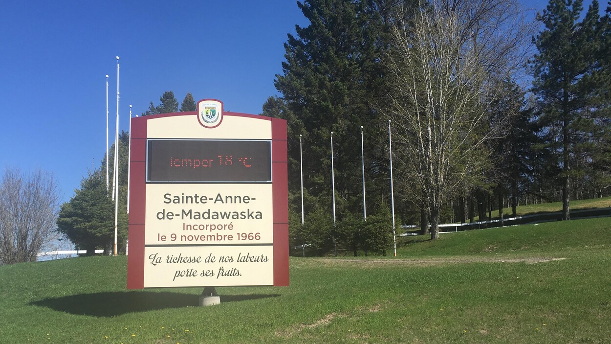 Dans un parc, l'enseigne à l'effigie du village de Sainte-Anne-de-Madawaska sur laquelle on peut lire : Incorporé le 9 novembre 1966. Le slogan du village : « La richesse de nos labeurs porte ses fruits ».