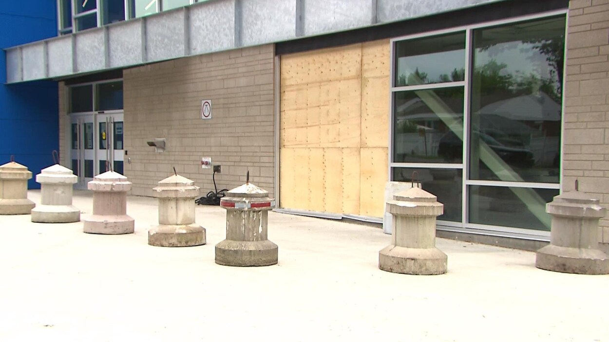 Des bornes en béton devant une façade réparée au contreplaqué.