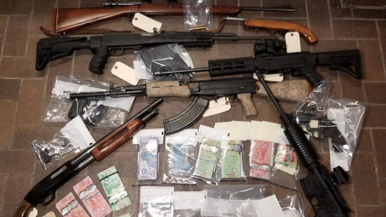 Des armes à feu de gros calibre et d'importantes sommes d'argent disposées sur un plancher.