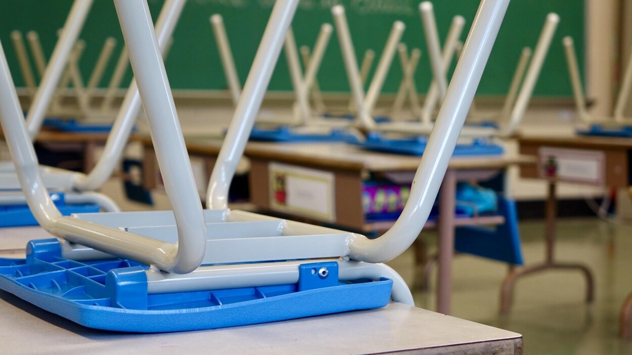 Des chaises sont retournées sur les pupitres d'une salle de classe sans élèves.
