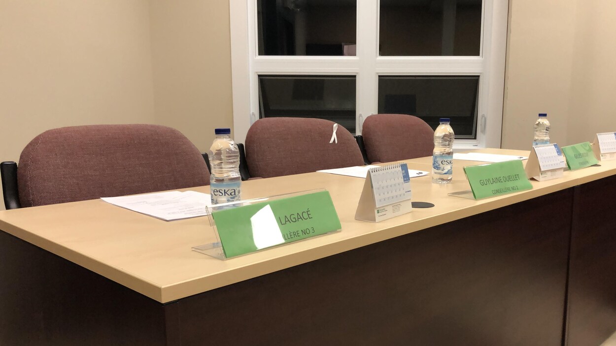 Les trois chaises vides derrière la table où se trouve des marques-places indiquant les noms de conseillers.