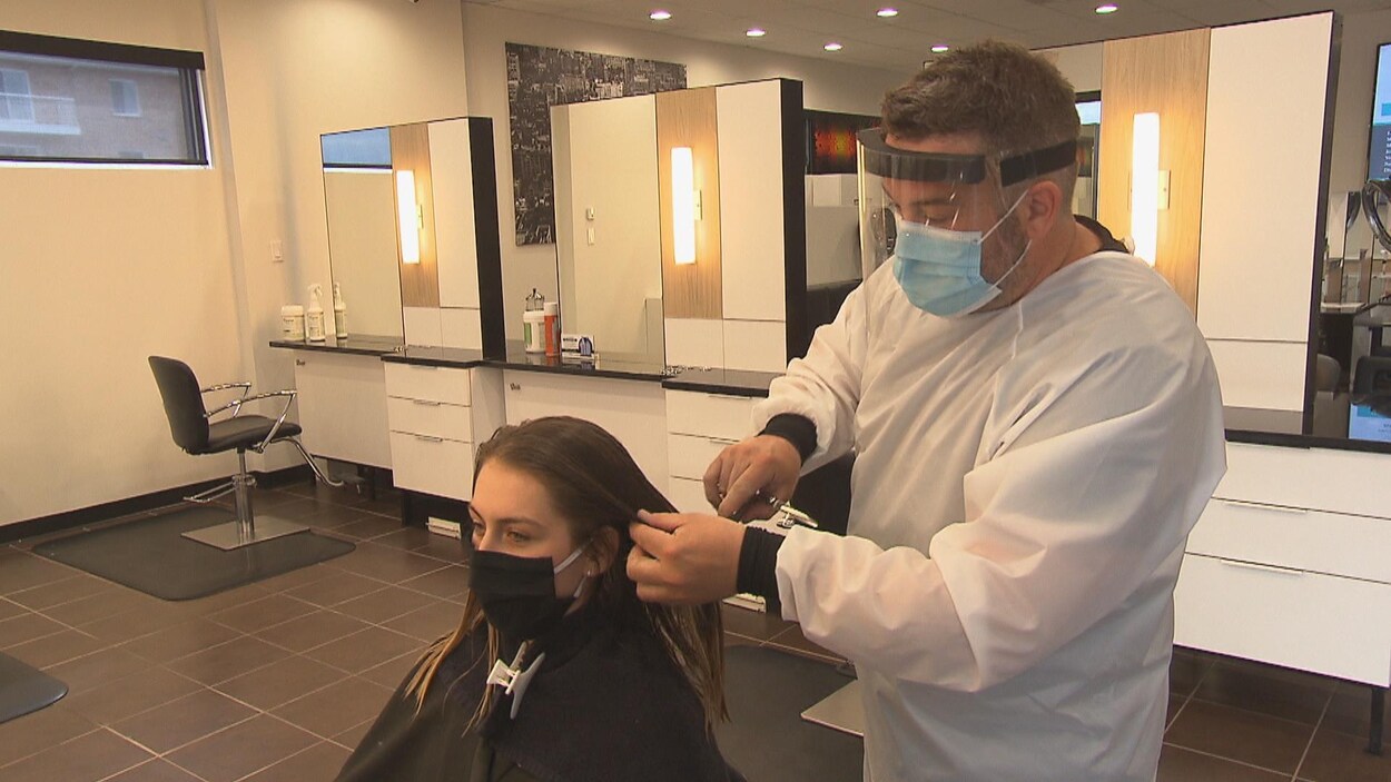 Un coiffeur coupe les cheveux d'une cliente.
