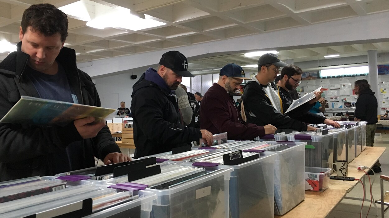 Des gens regardent des disques qui ont été disposés dans des caisses en plastique.