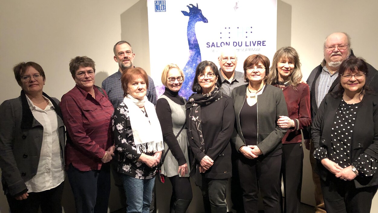 Un groupe de personnes se tient devant une affiche avec le logo du Salon du livre en Abitibi-Témiscamingue.