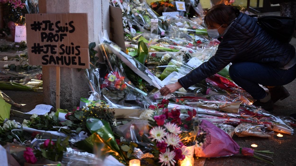 Une femme dépose une gerbe de fleurs au milieu de dizaines d'autres.