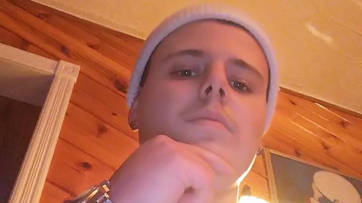 Gros plan d'un jeune homme qui porte un bonnet et des boucles d'oreilles.