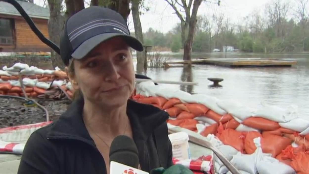 Une femme répond au micro de Radio-Canada devant les crues et les sacs de sable.