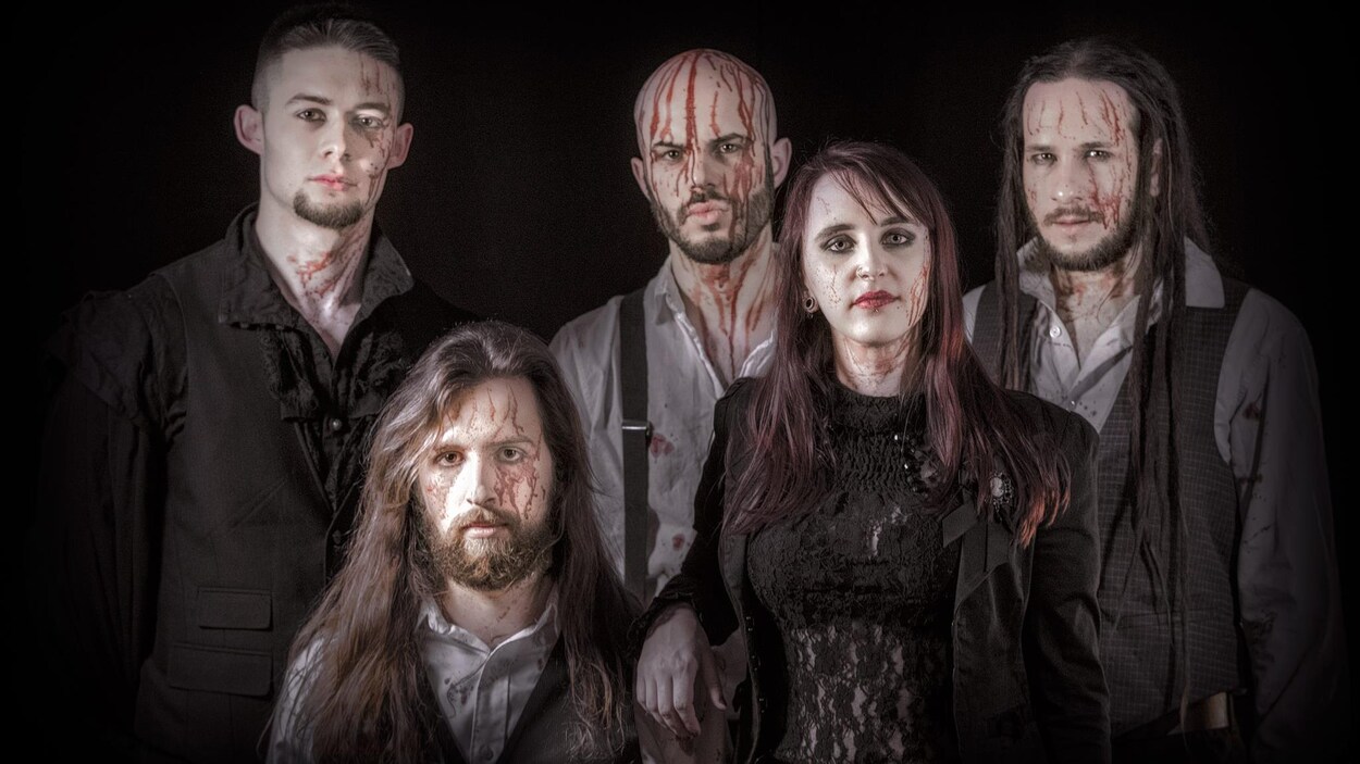 Cinq membres d'une formation metal, 4 gars, 1 fille, posent devant la caméra avec un air sérieux. Ils sont habillés de vêtements gothiques et il y a du sang sur leur visage.