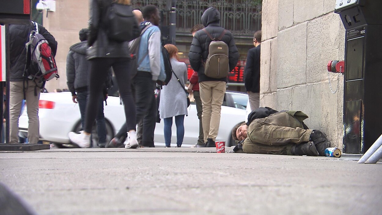 Un homme est couché sur un trottoir. Des passants marchent près de lui.