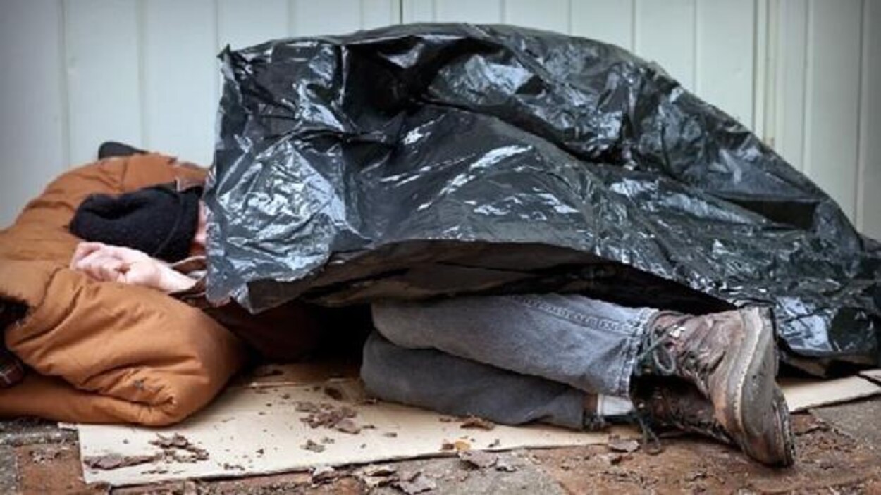 Un sans-abri dort à l'extérieur sur un carton, un sac de poubelle en guise de couverture.