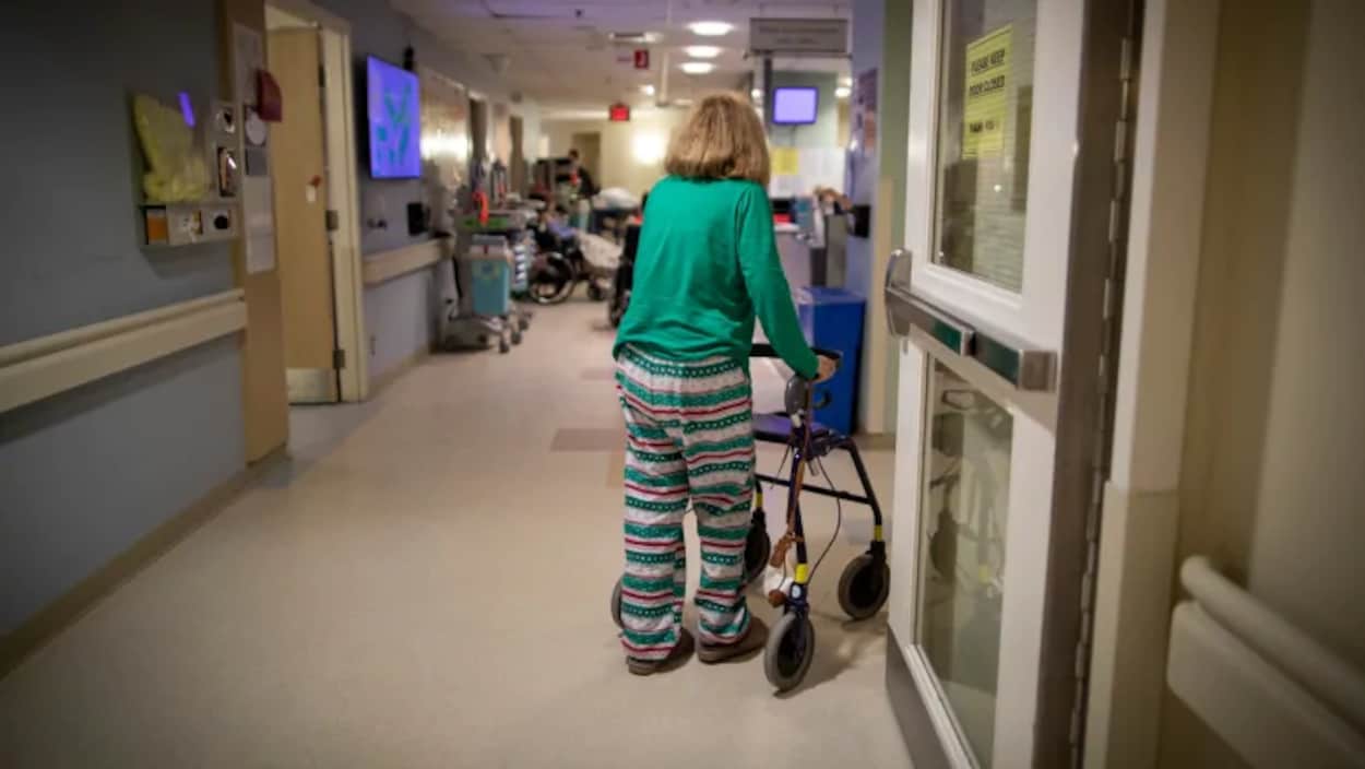 Une femme marche dans un corridor à l'aide d'un déambulateur.