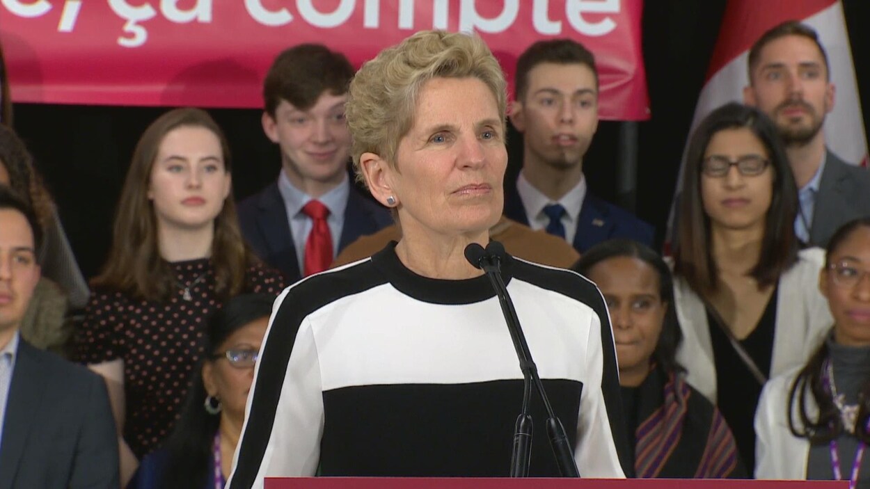 Photo de Kathleen Wynne habillée en noir et blanc devant un micro. Photo de Kathleen Wynne habillée en noir et blanc devant un micro.