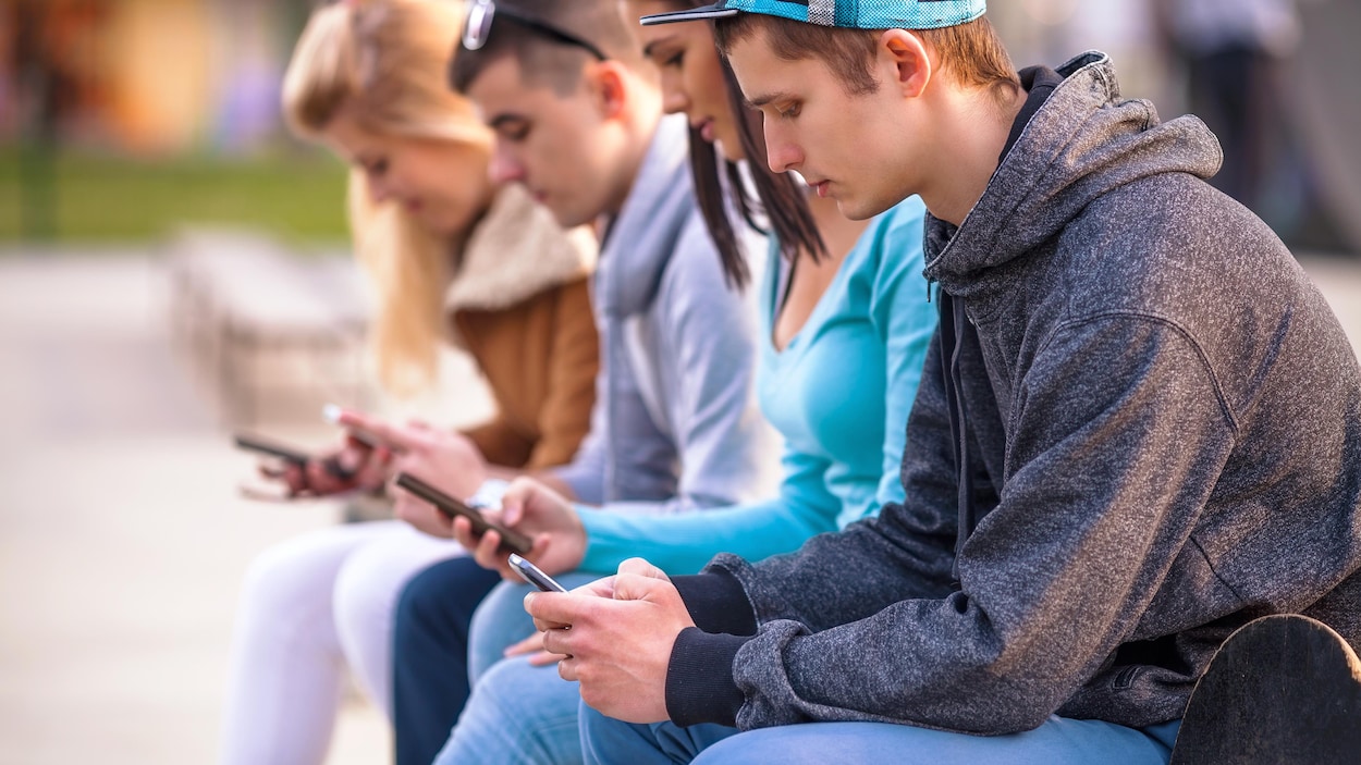 Quatre adolescents assis à l'extérieur regardent leurs téléphones cellulaires.